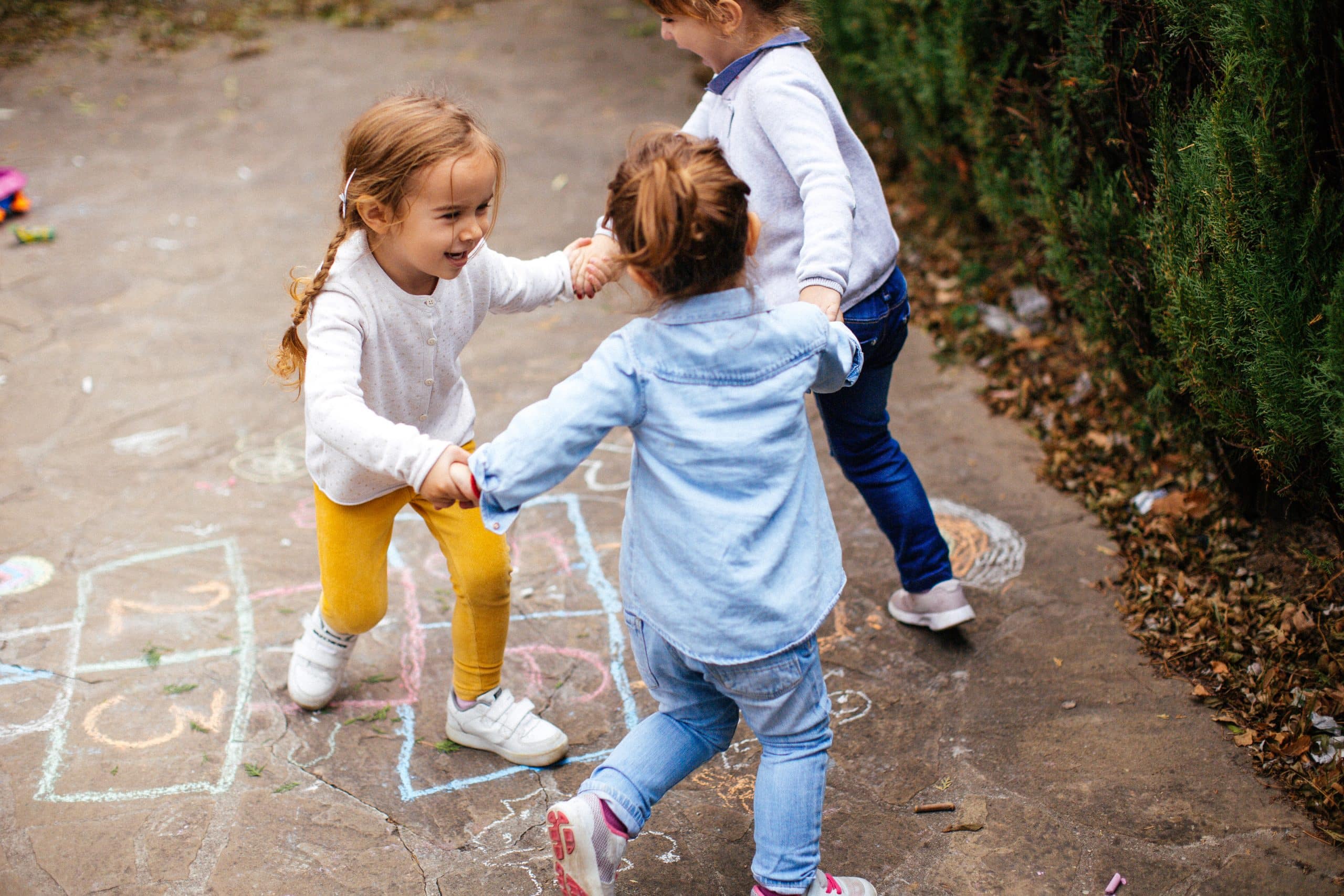 Drie kleuters doen een hinkelspel op het schoolplein.